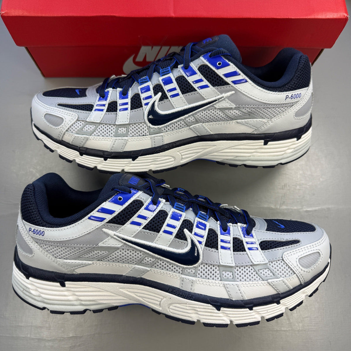 Nike P-6000 grey trainers with blue and white accents, featuring logo detail.