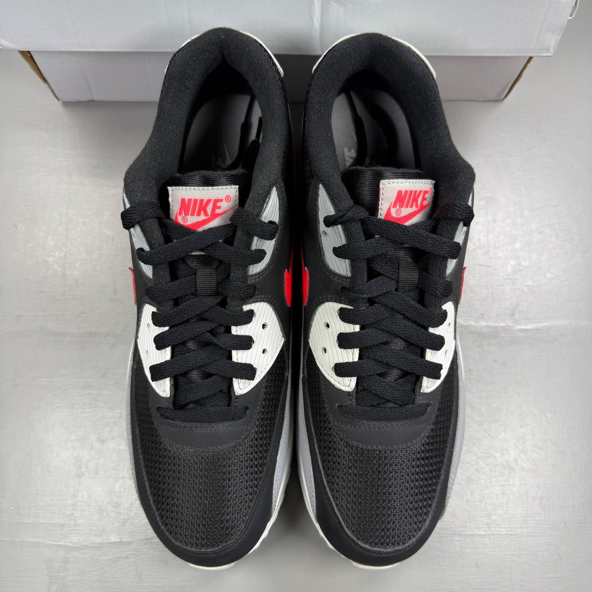 Nike Air Max 90 black sneakers with bright crimson accents and logo detailing.