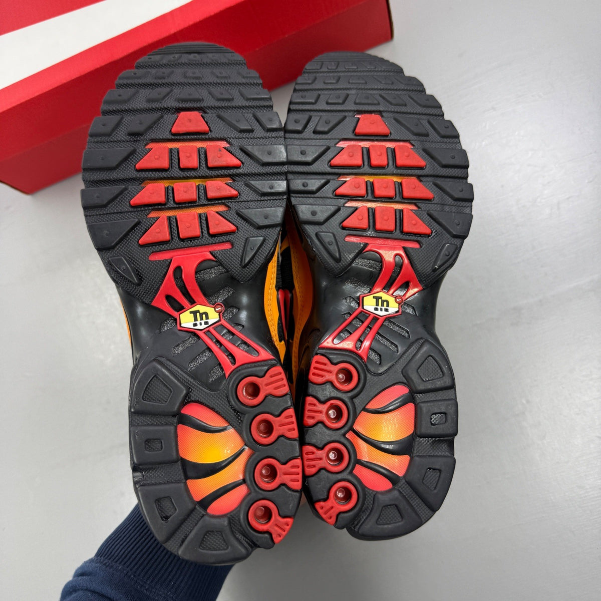 Nike black Air Max Plus TN trainers with red and orange accents and signature logo.