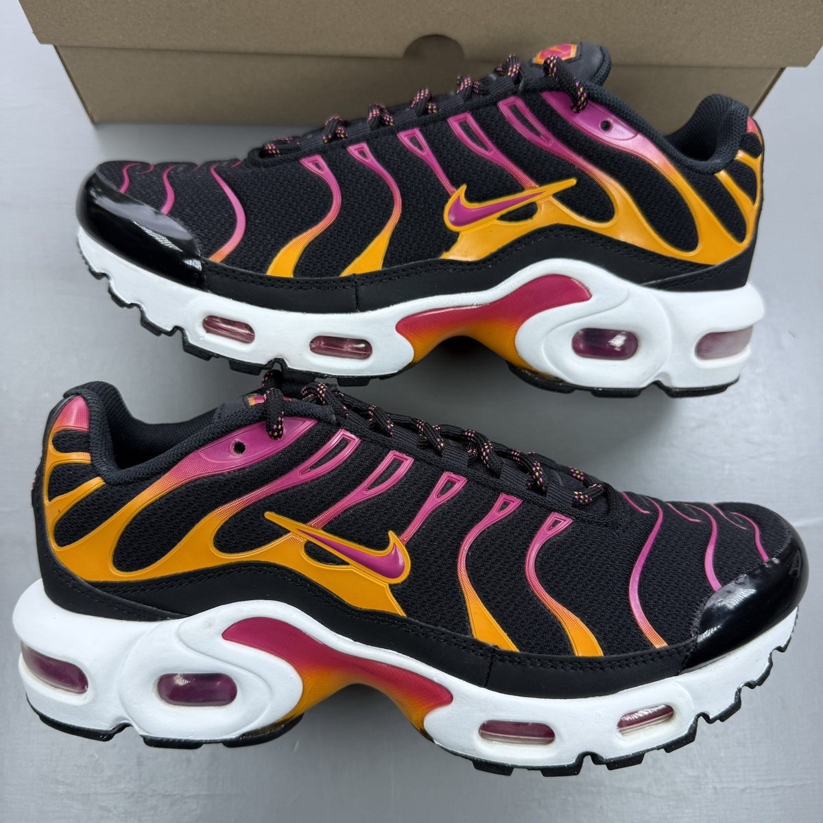 Nike Air Max Plus TN black trainers with active pink and white accents, logo detailing.