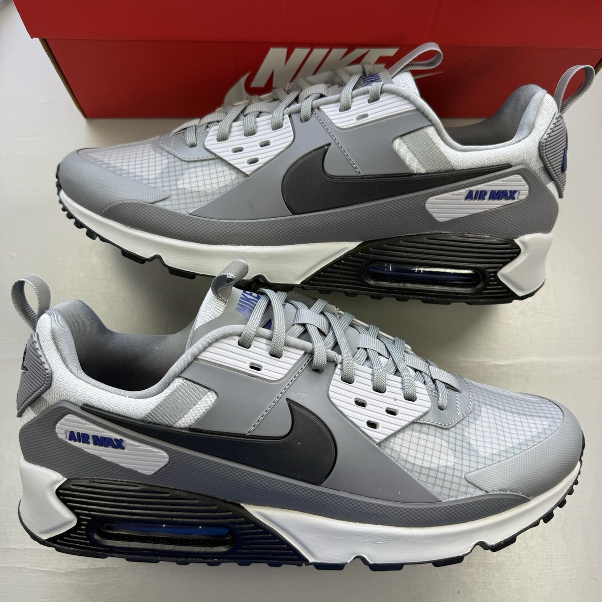Nike Air Max 90 Drift grey trainers with deep royal blue accents and logo details.