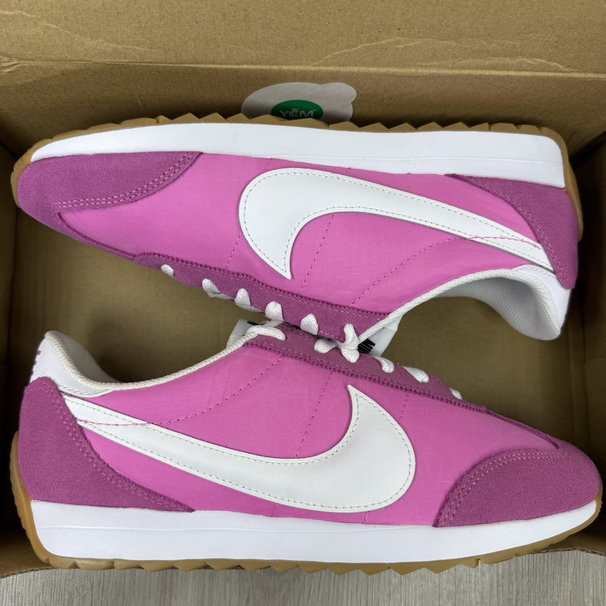Nike white trainers with pink accents and gum sole, featuring iconic swoosh logo.