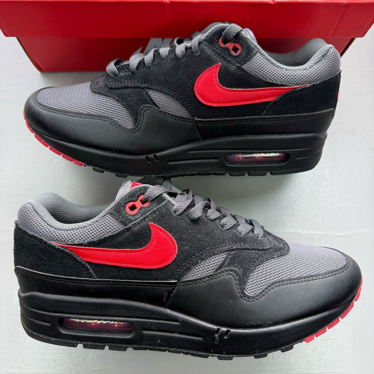 Nike black Air Max 1 trainers with red accents and logo detail.