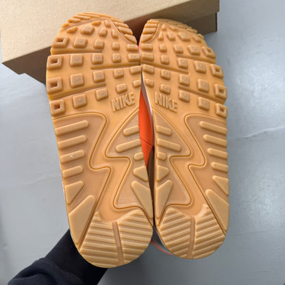Nike Air Max 90 orange trainers with white and gum sole, featuring iconic logo.