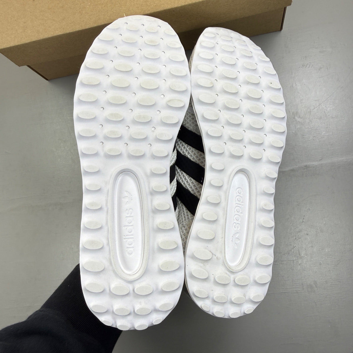 Adidas white trainers with black accents and iconic three stripes design.