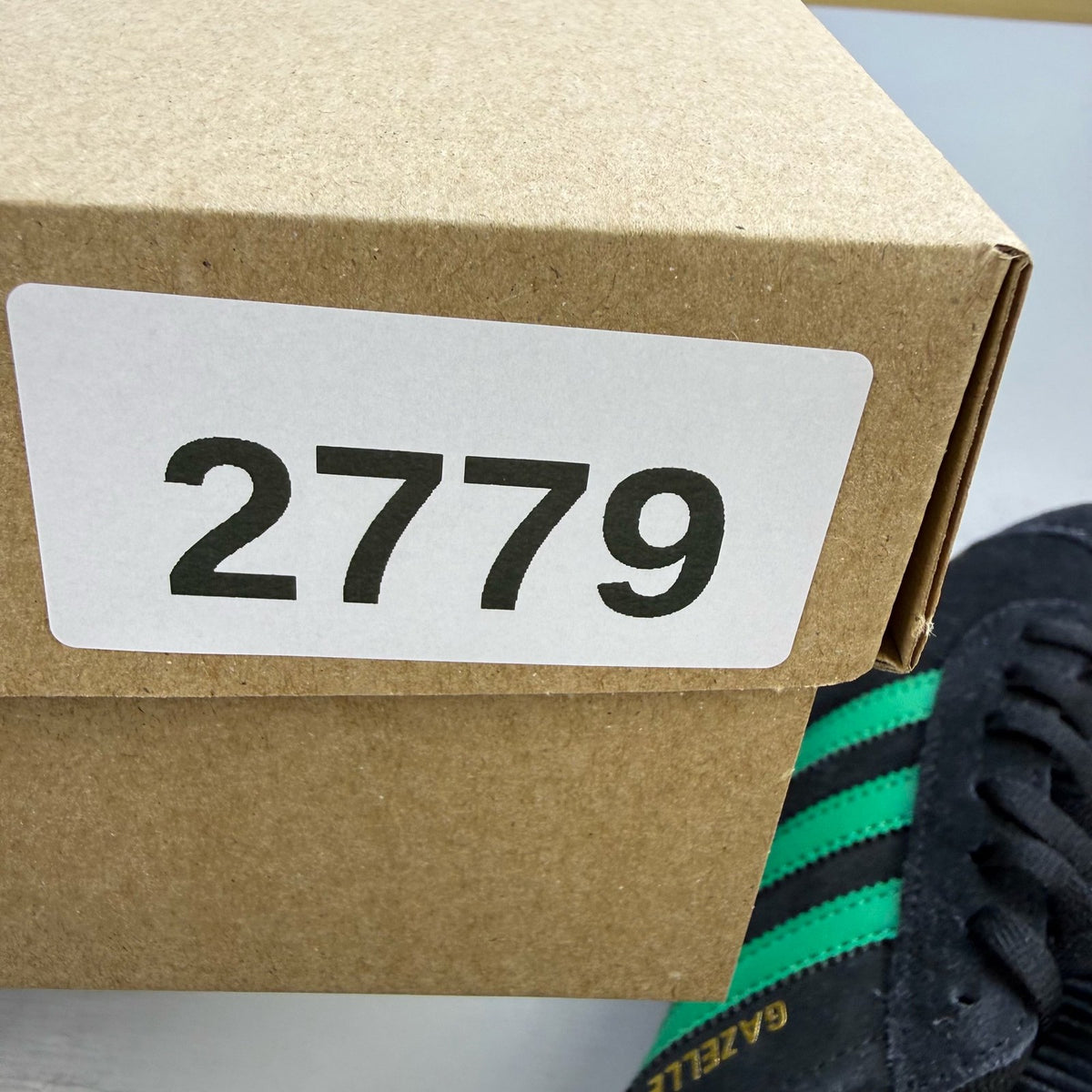 Adidas black Gazelle trainers with green accents and classic logo detailing.