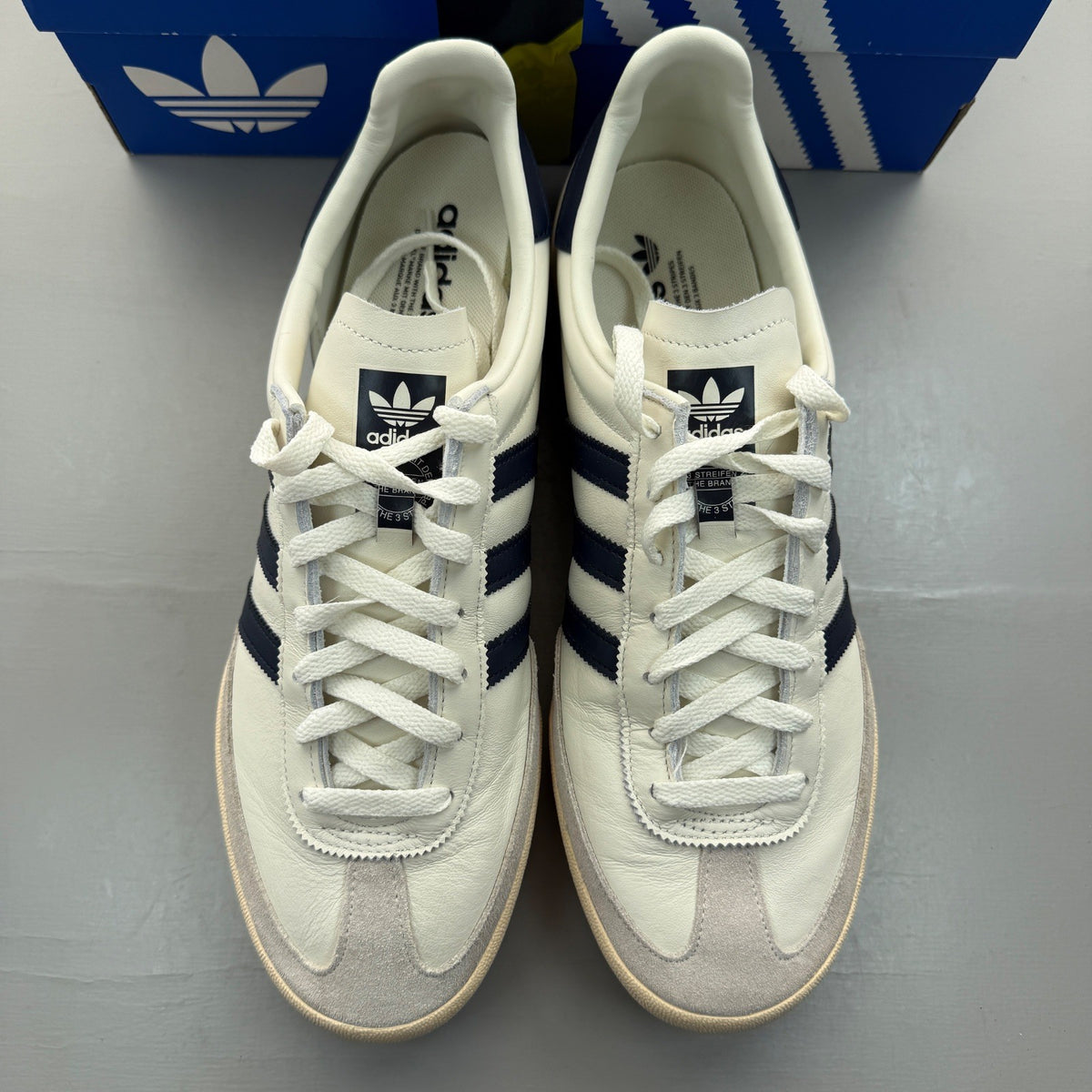Adidas white trainers with navy accents and leather detailing, featuring iconic logo.