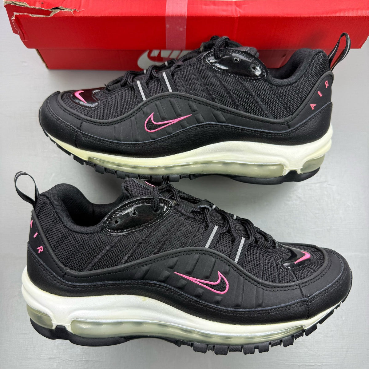 Nike Air Max 98 black trainers with crimson and pink accents, mesh and leather material.