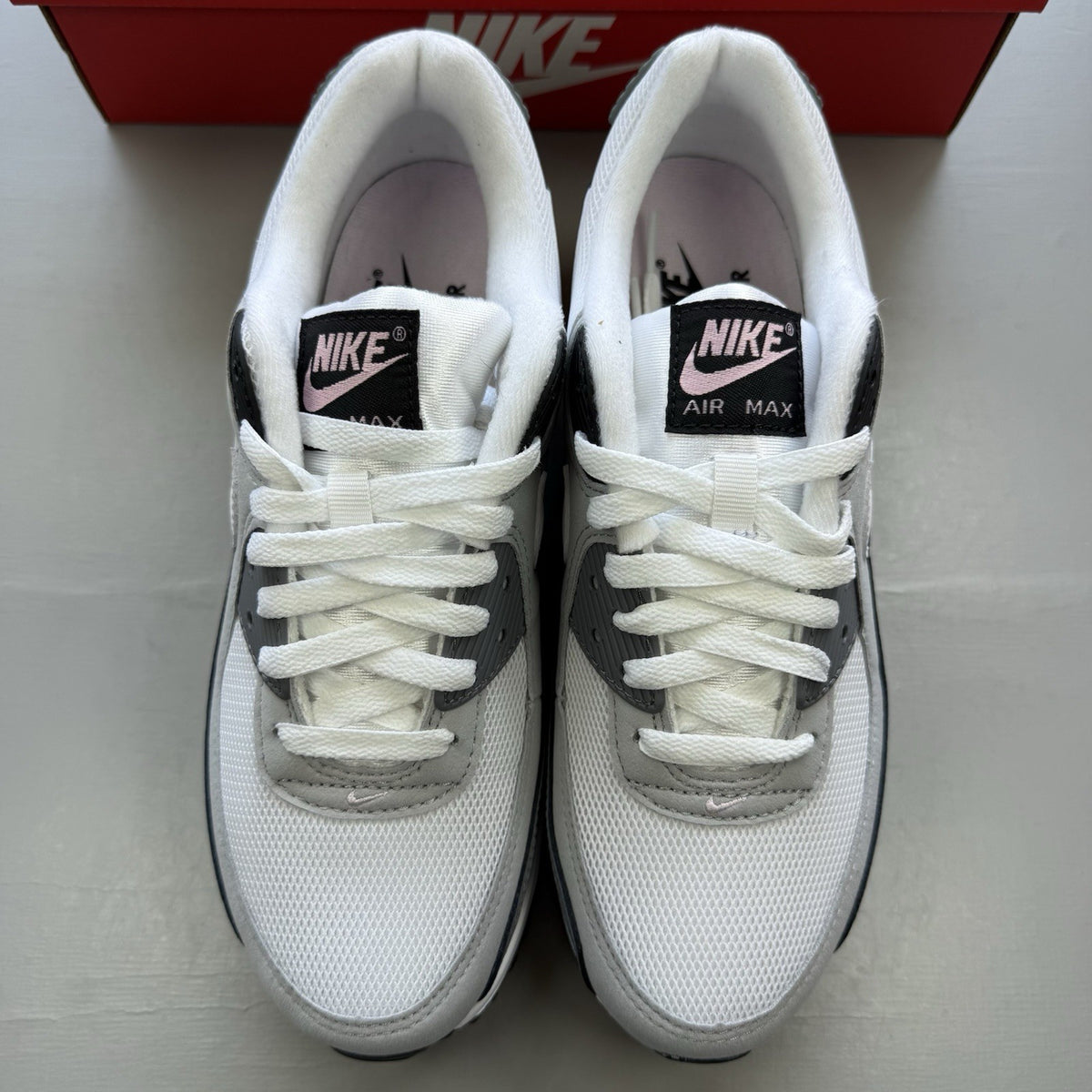 Nike Air Max 90 white trainers with pink foam accents and grey detailing.