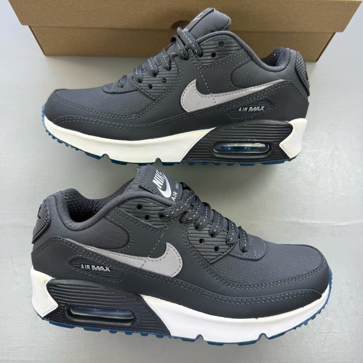 Nike Air Max 90 grey trainers with blue accents and logo detailing.