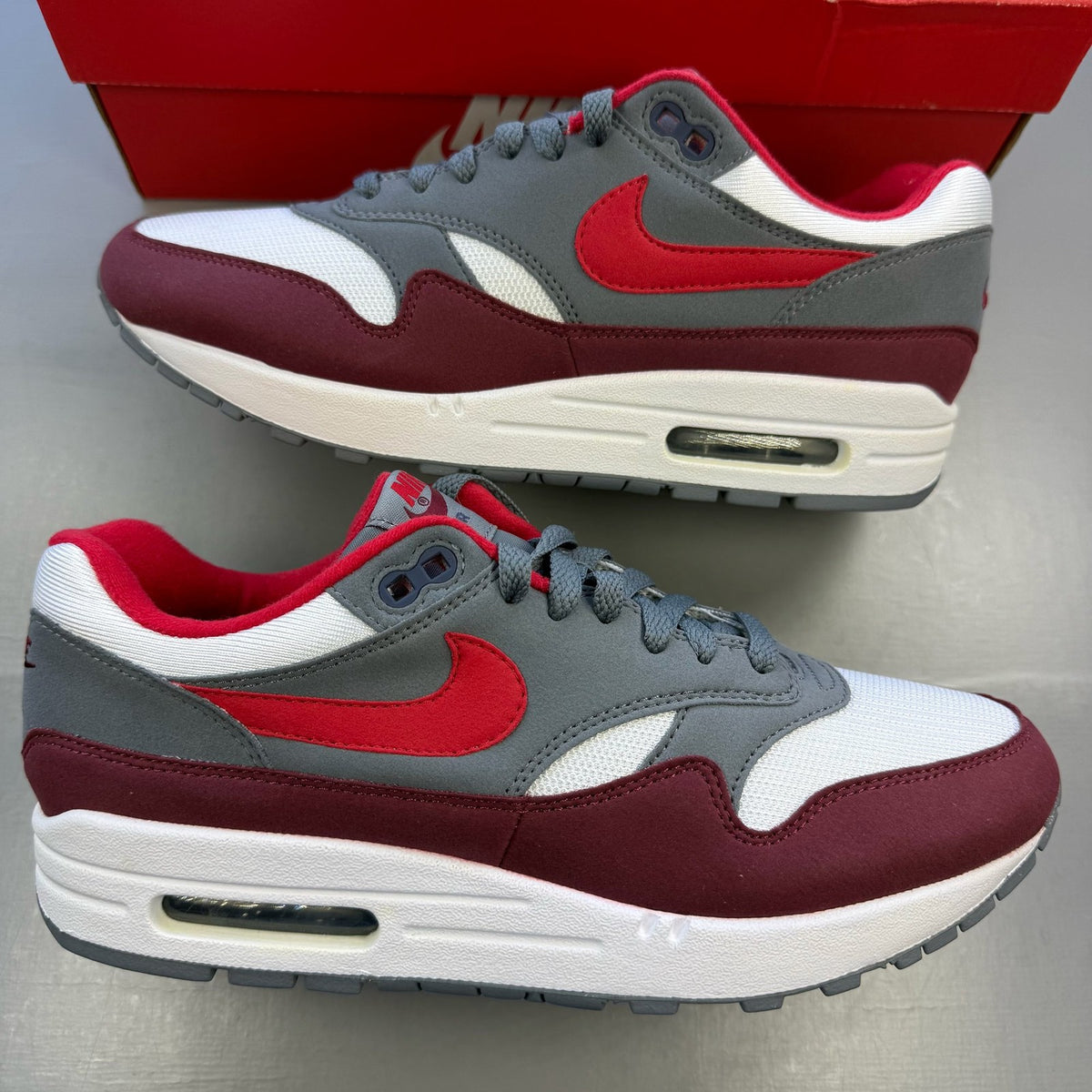 Nike Air Max 1 trainers grey red white with logo and mesh material details.