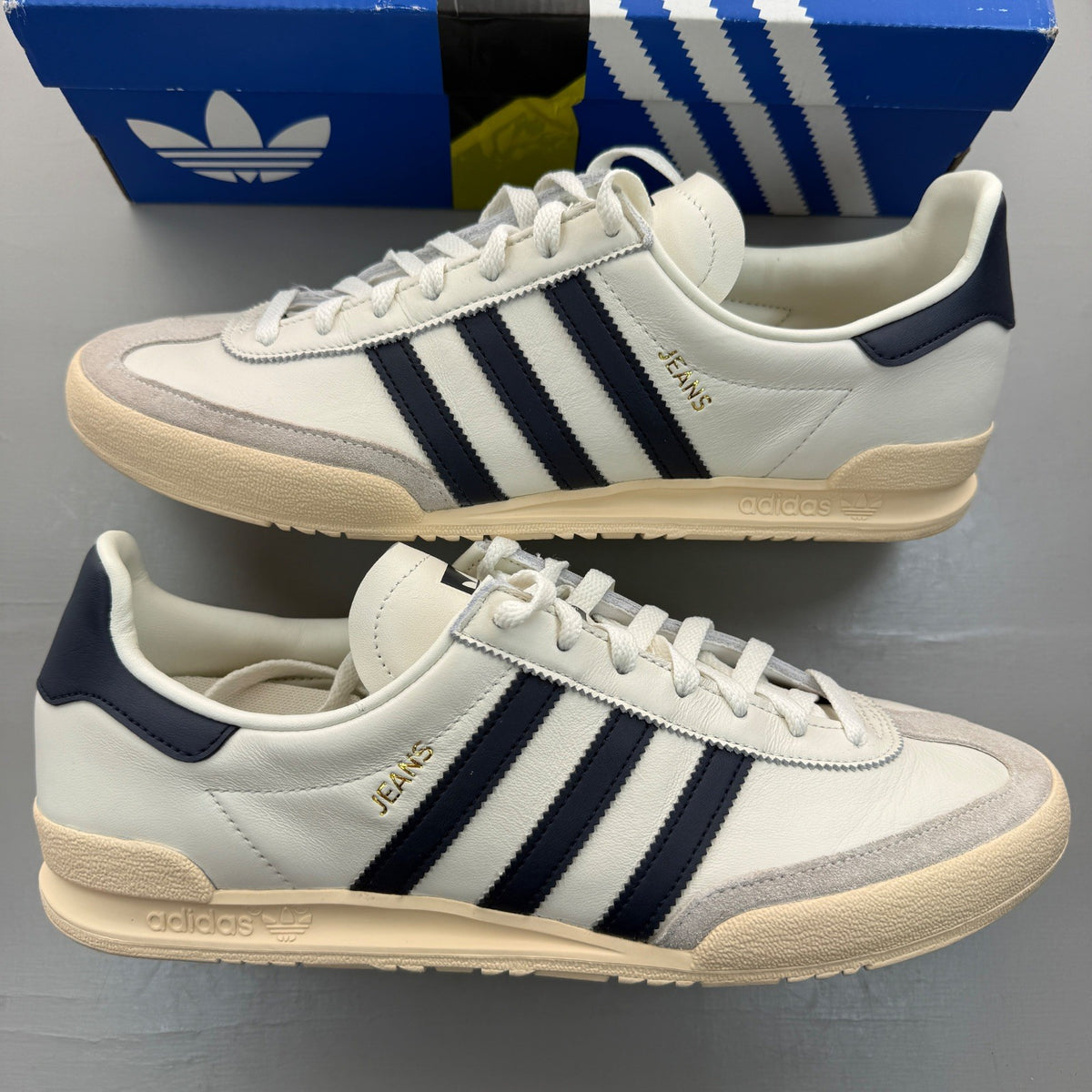 Adidas white trainers with navy accents and leather detailing, featuring iconic logo.