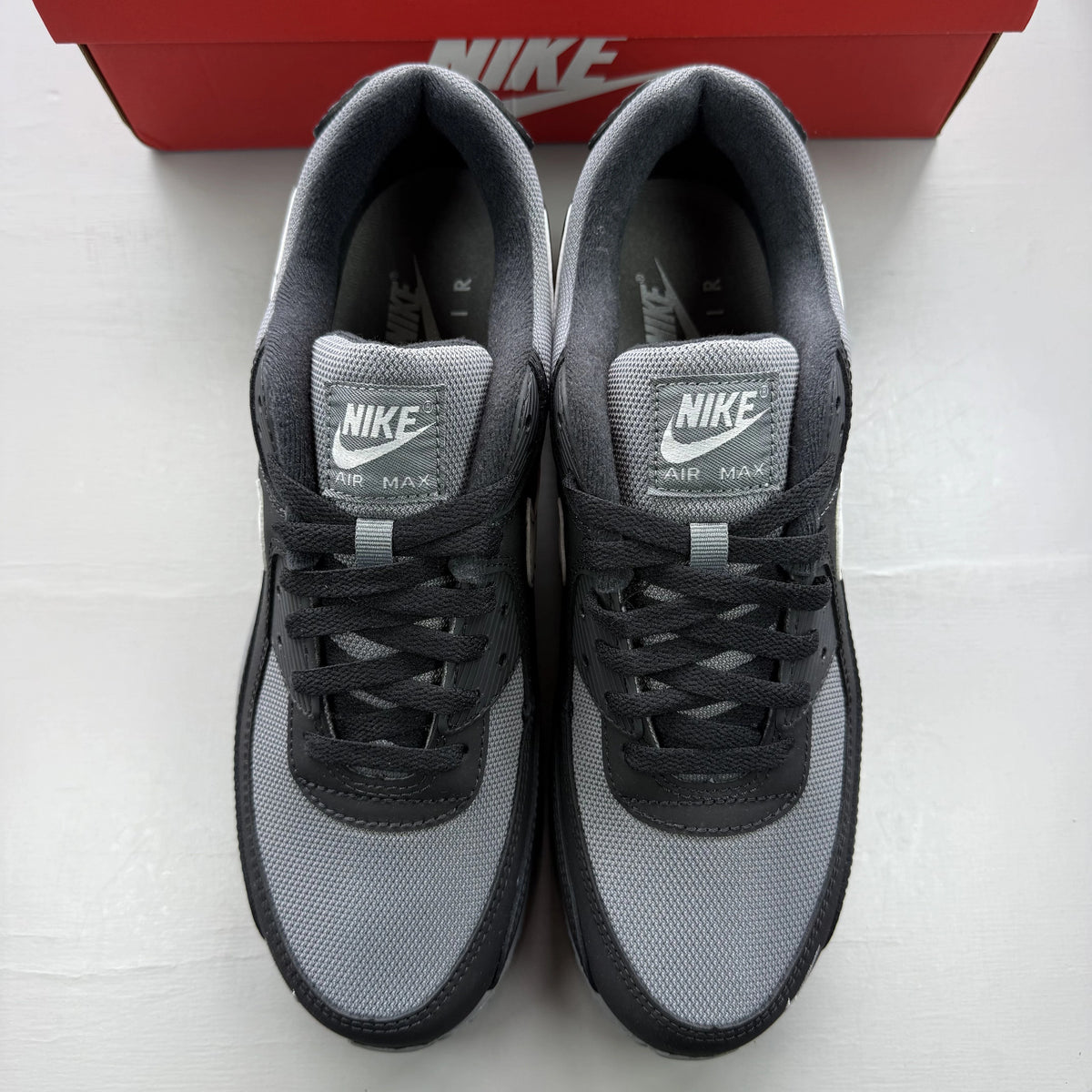 Nike Air Max 90 black trainers with smoke grey accents and logo detail.