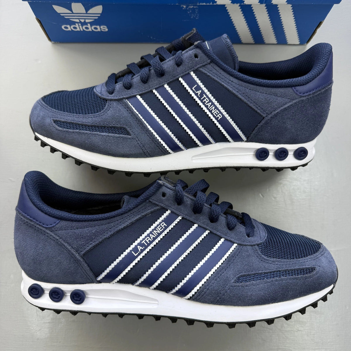 Adidas blue LA Trainer sneakers with white stripes and logo detailing.