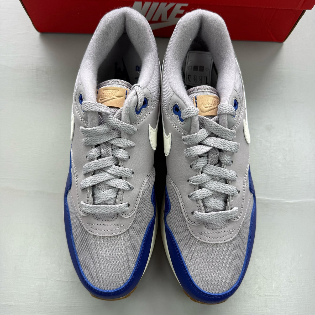 Nike Air Max 1 grey trainers with royal blue accents and signature logo.