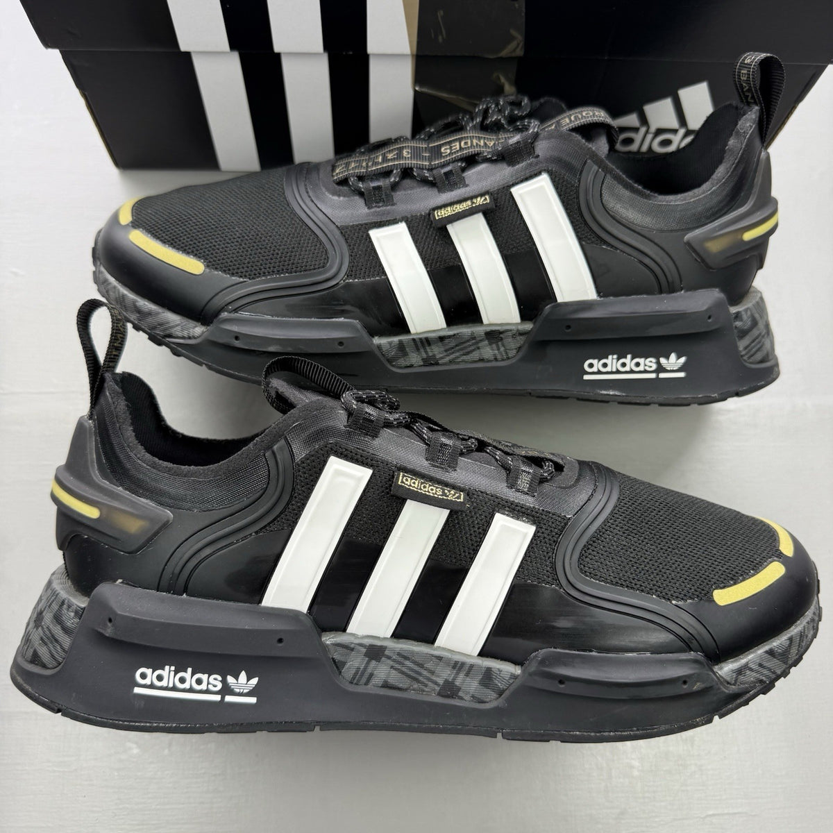 Adidas black trainers with white and gold accents, featuring a sleek design and logo.