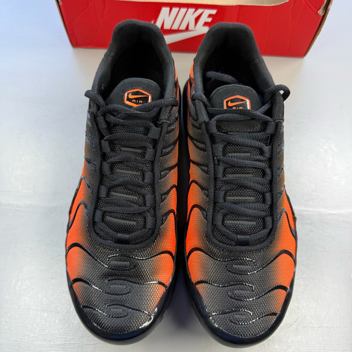 Nike Air Max Plus TN black trainers with orange accents and signature logo details.