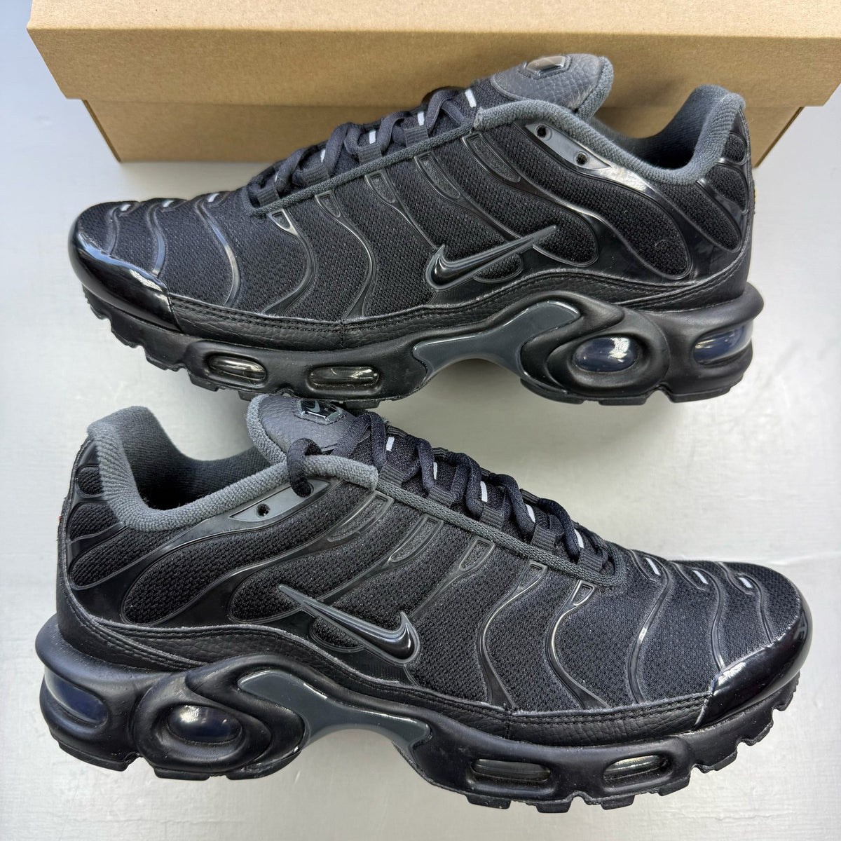 Nike Air Max Plus TN black trainers with dark smoke grey accents and logo detailing.
