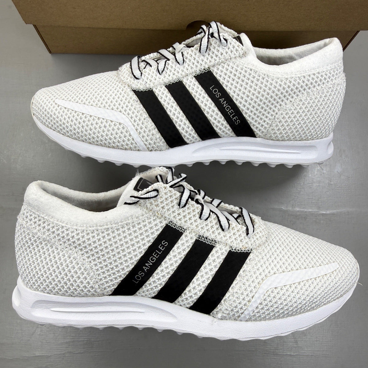 Adidas white trainers with black accents and iconic three stripes design.