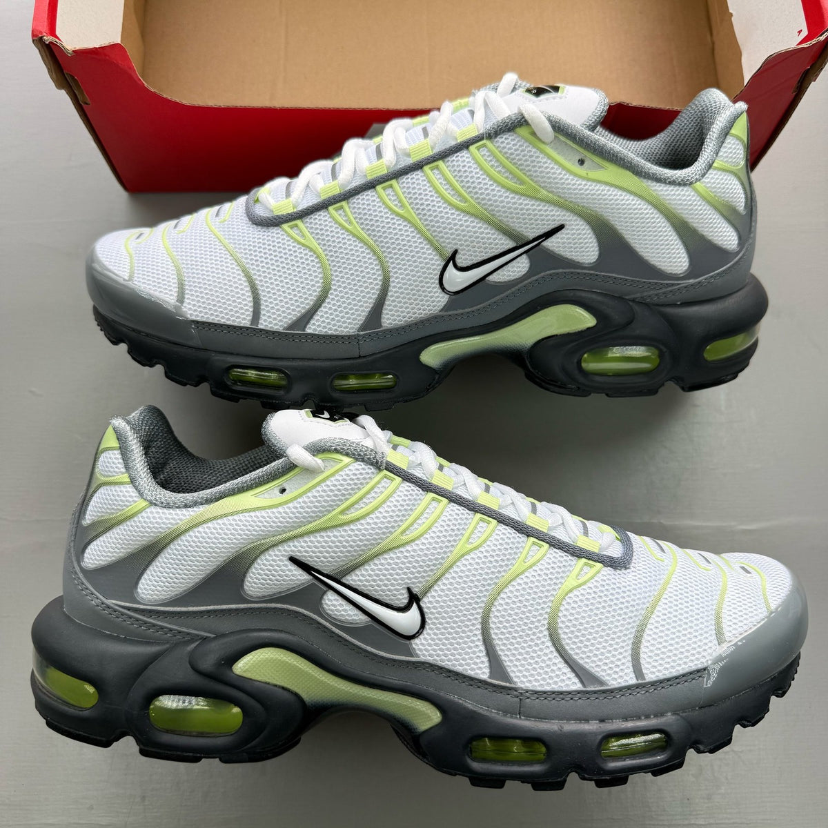 Nike Air Max Plus TN grey trainers with white and liquid lime accents, featuring logo details.