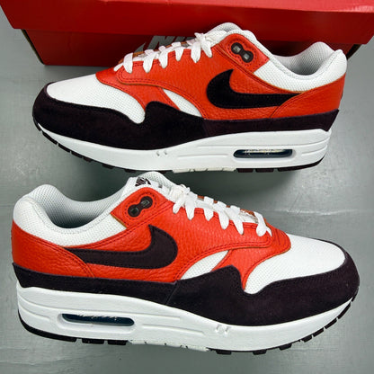 Nike Air Max 1 white trainers with burgundy accents and logo detail.