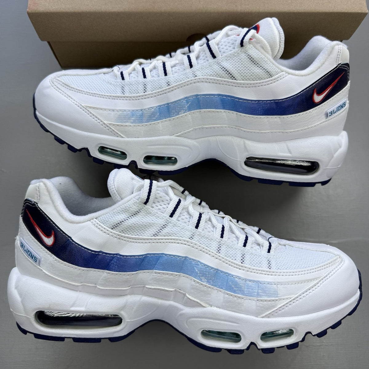 Nike Air Max 95 trainers white with blue and red accents, featuring iconic logo detailing.