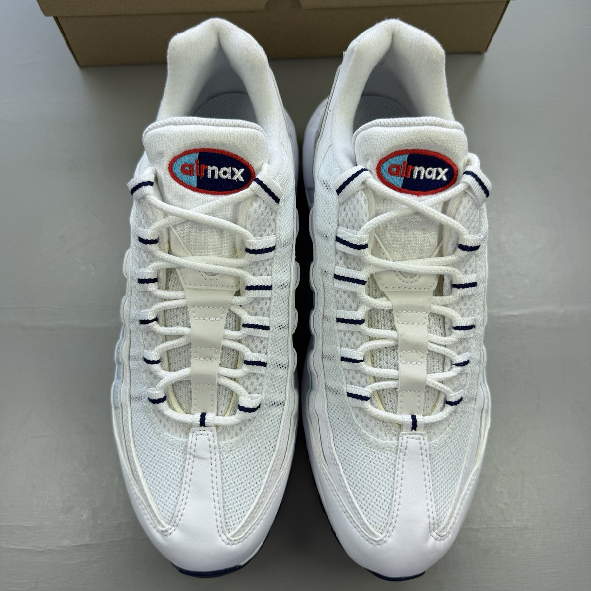 Nike Air Max 95 trainers white with blue and red accents, featuring iconic logo detailing.