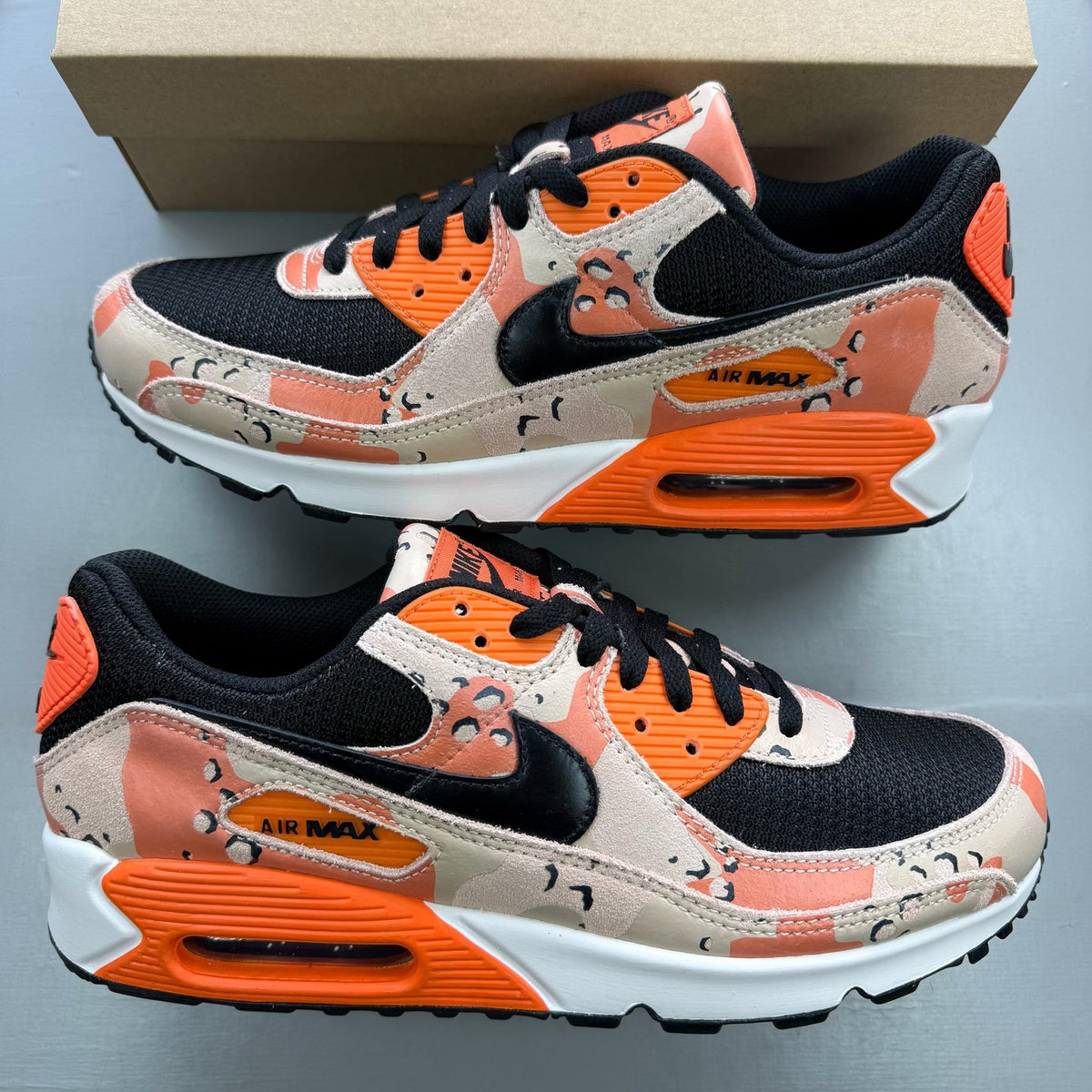 Nike black trainers with camo pattern and orange accents, featuring premium materials.