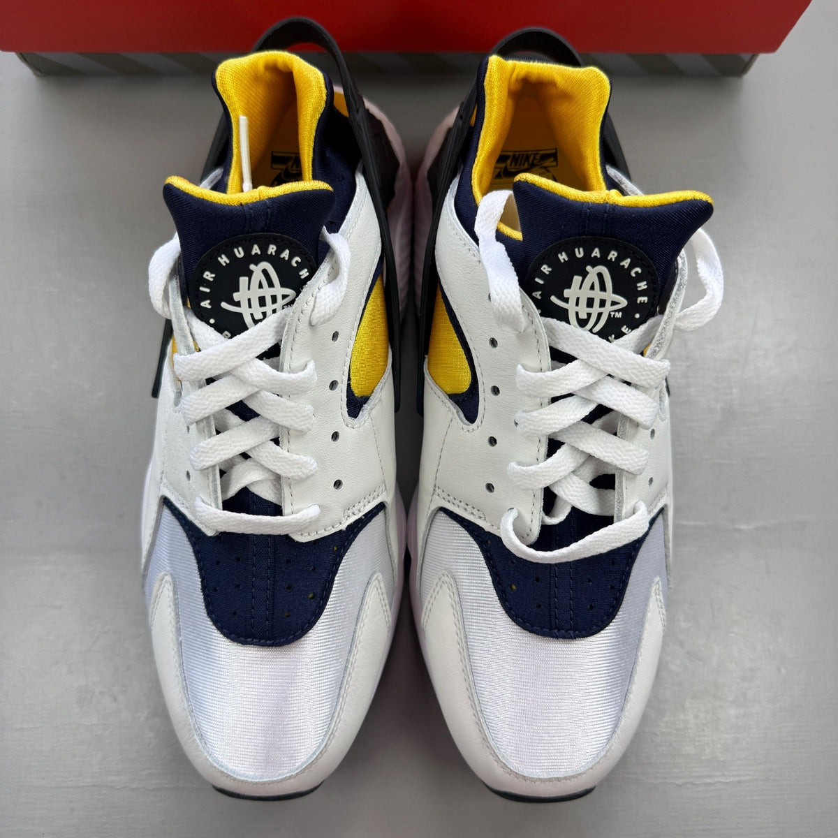 Nike athletic shoes white with yellow maize and navy accents, featuring iconic Huarache design.