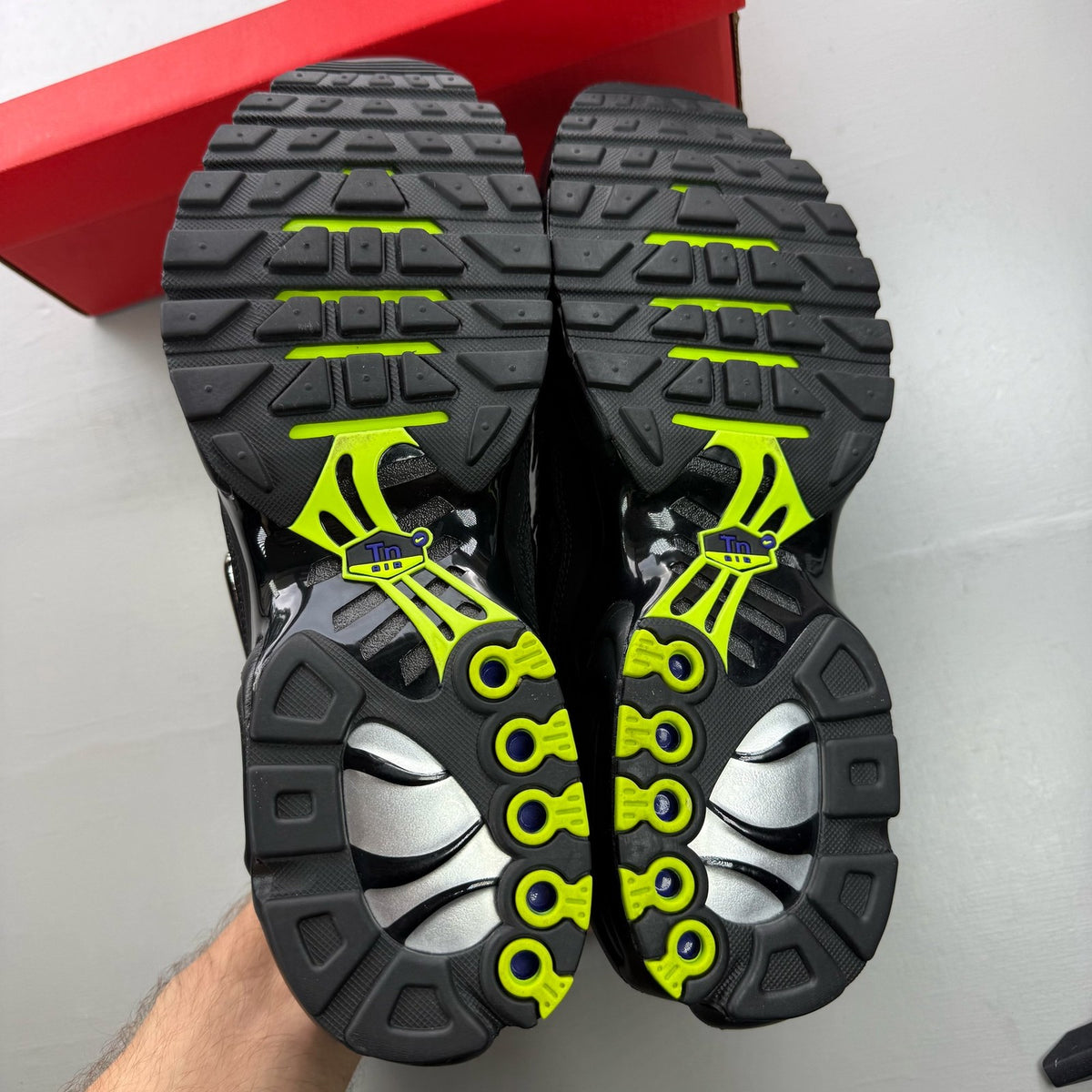 Nike black Air Max Plus TN trainers with chrome accents and vibrant volt detailing.