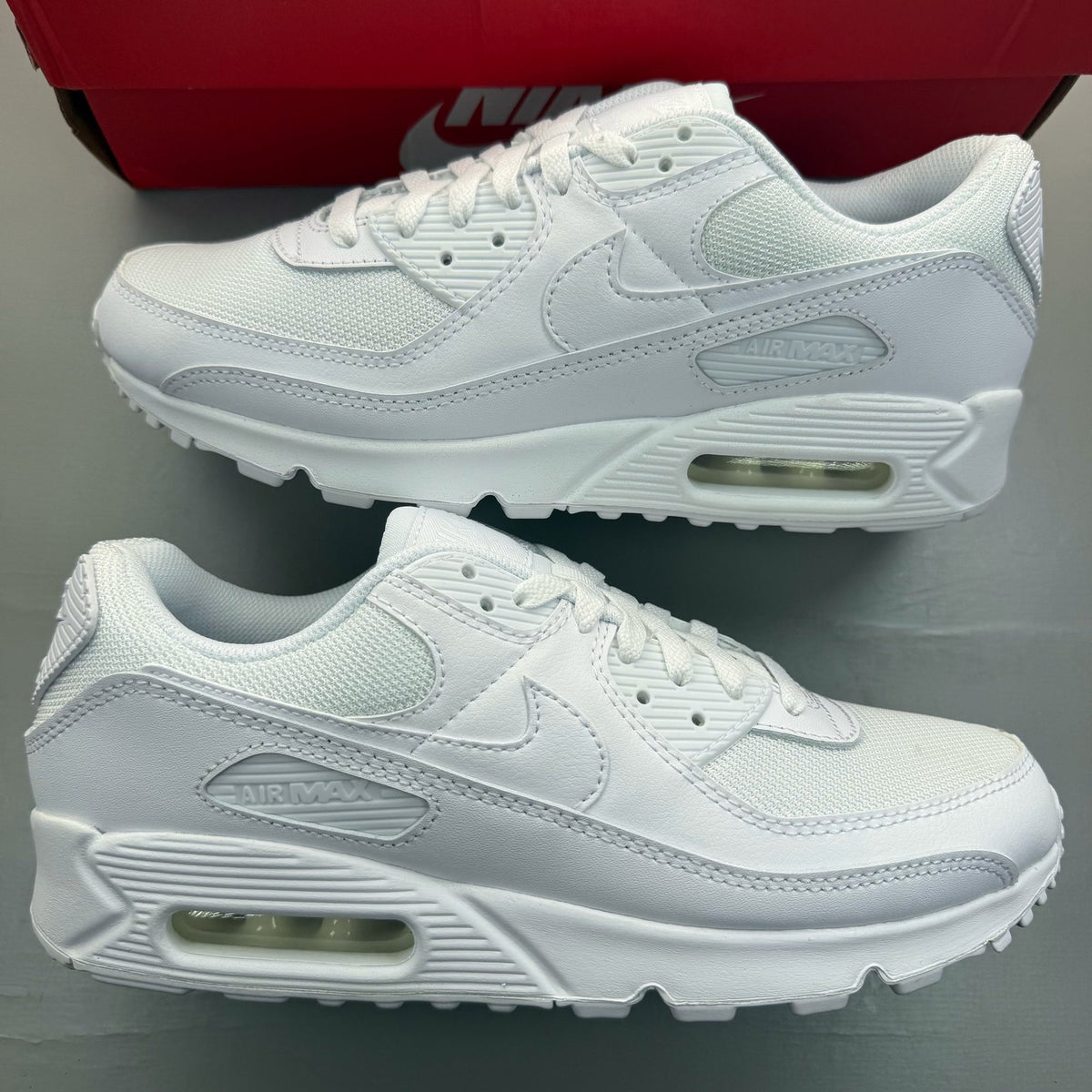 Nike Air Max 90 white trainers with iconic swoosh logo and breathable mesh material.
