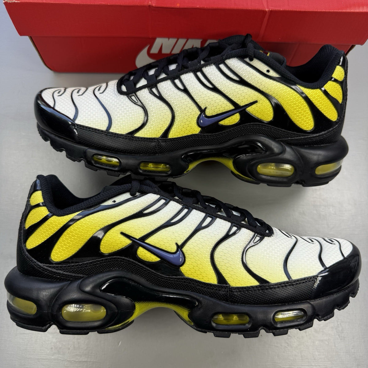 Nike Air Max Plus TN black trainers with bright citron yellow accents and signature logo.