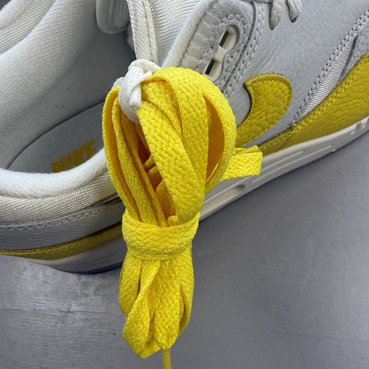 Nike Air Max 1 white trainers with yellow accents and grey detailing.