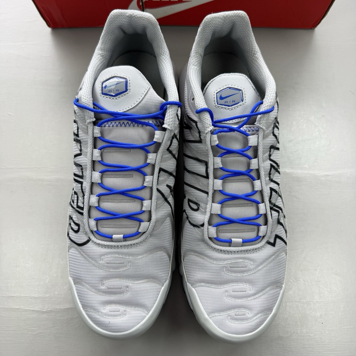 Nike Air Max Plus TN trainers grey with blue accents and signature swoosh logo.