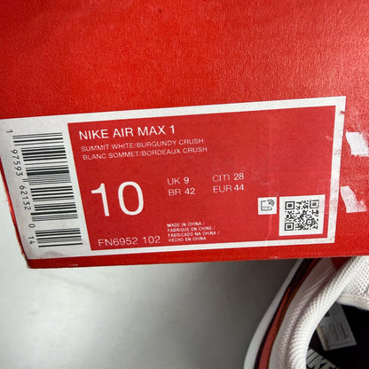 Nike Air Max 1 white trainers with burgundy accents and logo detailing.
