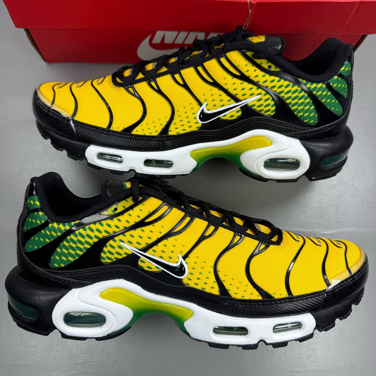 Nike Air Max Plus trainers yellow with pine green accents and logo detail.