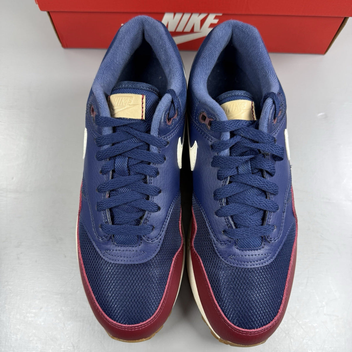Nike Air Max 1 red trainers with navy accents and gum sole, featuring logo details.