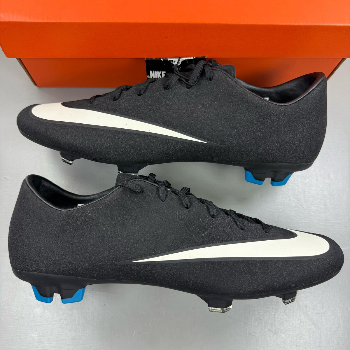 Nike black football boots with white Mercurial logo, sleek design, synthetic material.