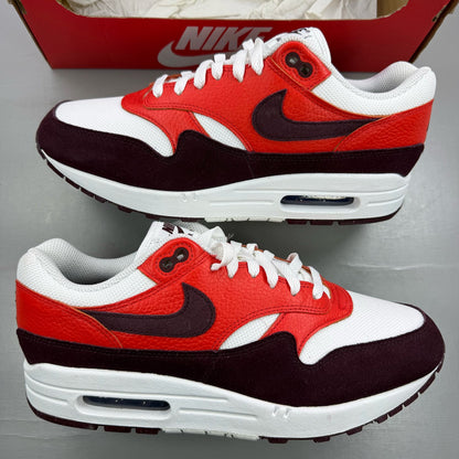 Nike Air Max 1 white trainers with burgundy accents and logo detailing.