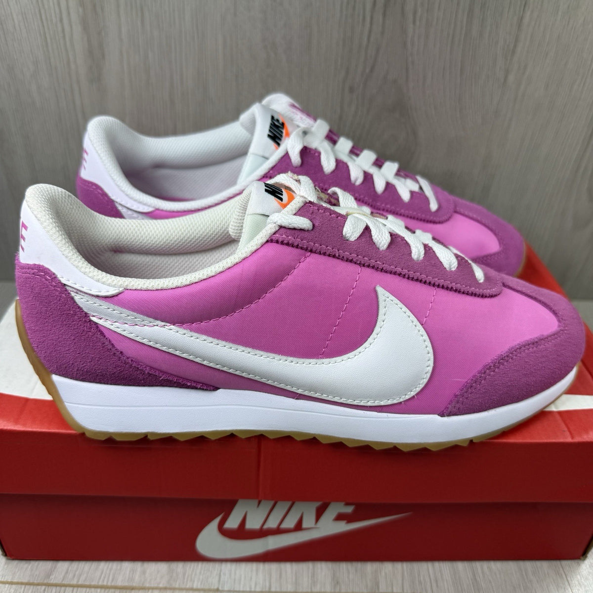Nike white trainers with pink accents and gum sole, featuring iconic swoosh logo.