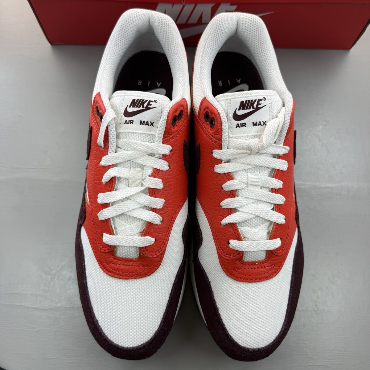 Nike Air Max 1 white trainers with burgundy and red accents, featuring logo details.