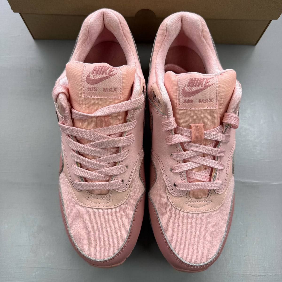 Nike Air Max 1 pink trainers with white accents and logo details.