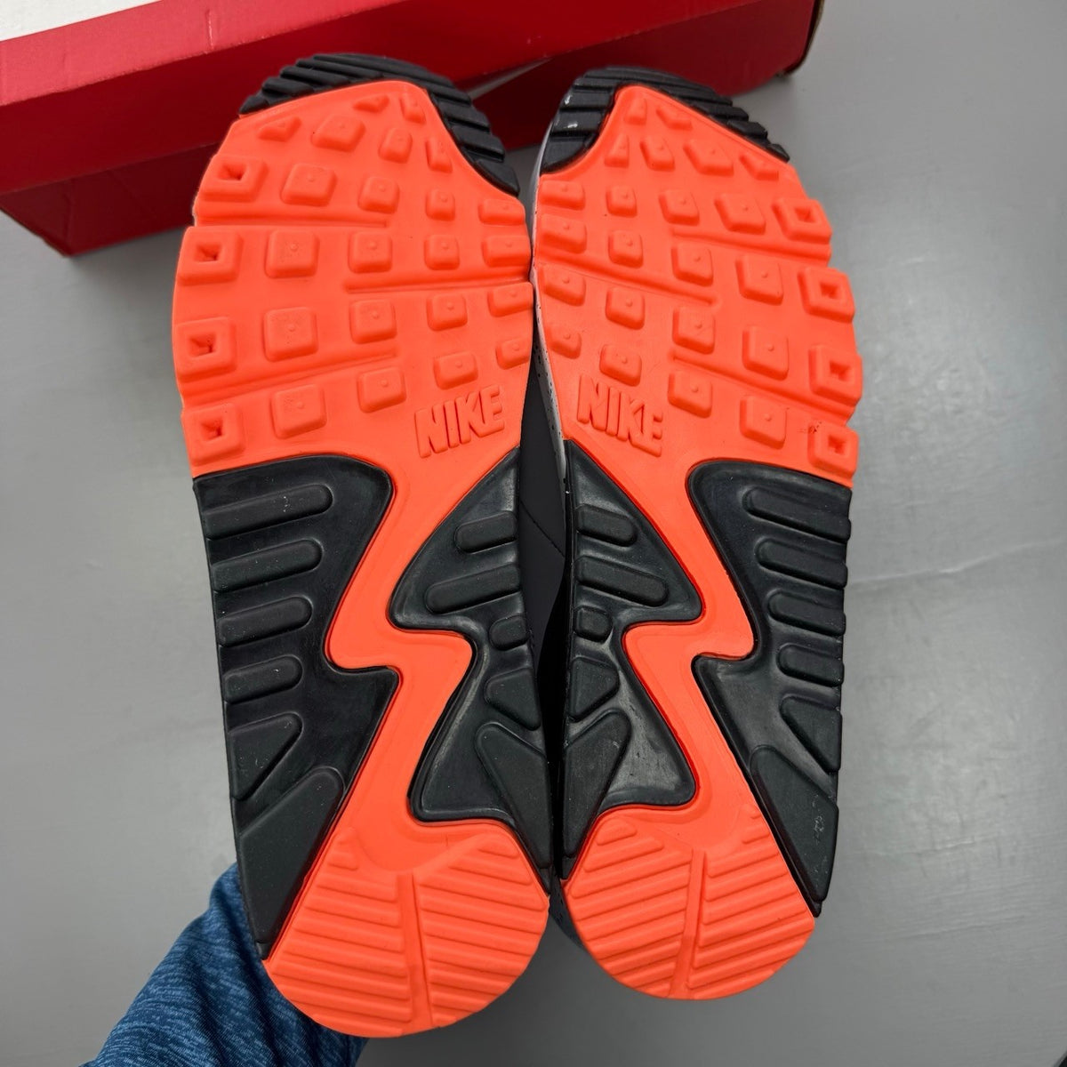 Nike Air Max 90 black trainers with turf orange and white accents, featuring logo details.