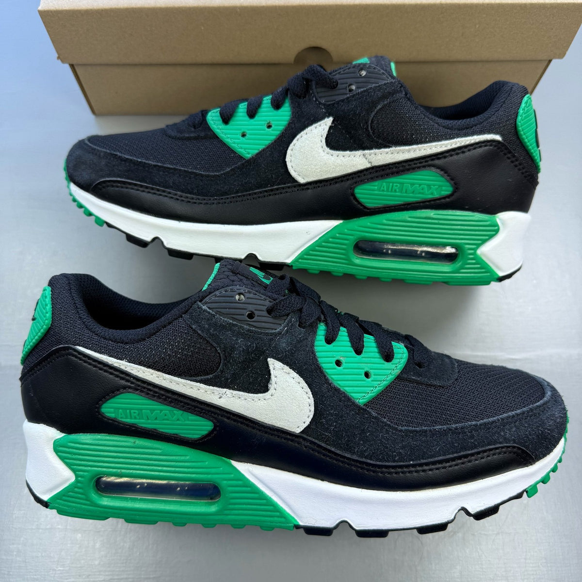 Nike Air Max 90 black trainers with green accents and white sole, featuring logo details.