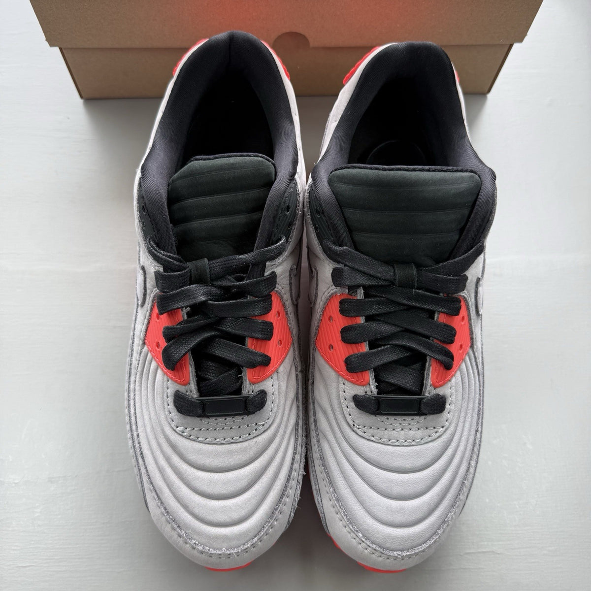 Nike Air Max 90 grey trainers with bright crimson accents and black detailing.