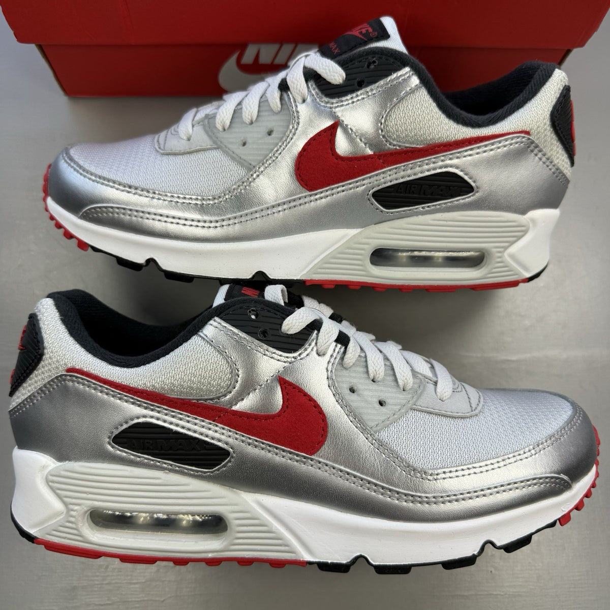 Nike Air Max 90 Icons grey trainers with red accents and white sole, featuring logo details.