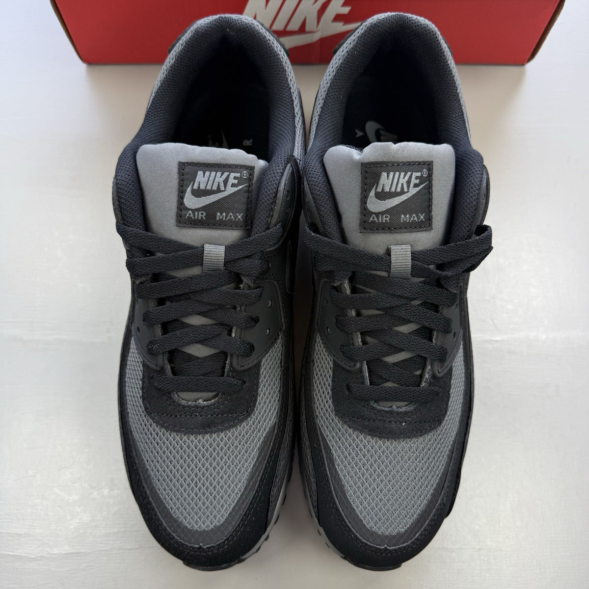 Nike Air Max 90 black trainers with grey accents and iconic logo detail.