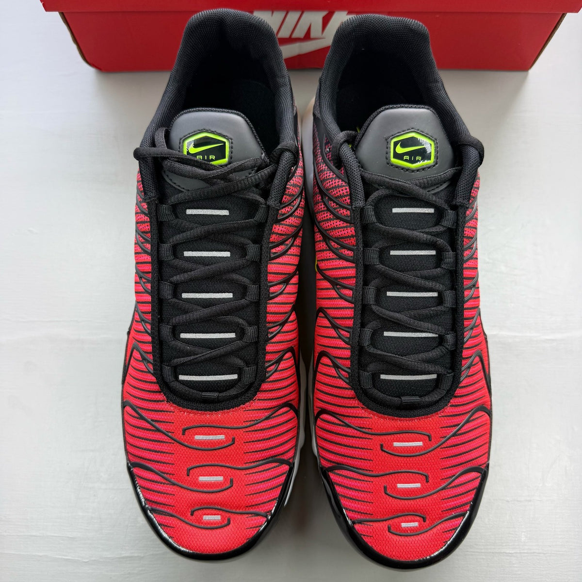 Nike Air Max Plus TN red trainers with black accents and vibrant volt detailing.