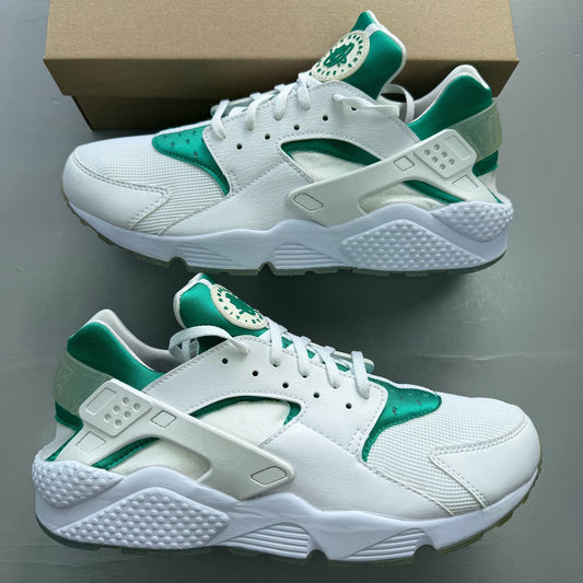 Nike Air Huarache white trainers with green accents and distinctive logo detailing.