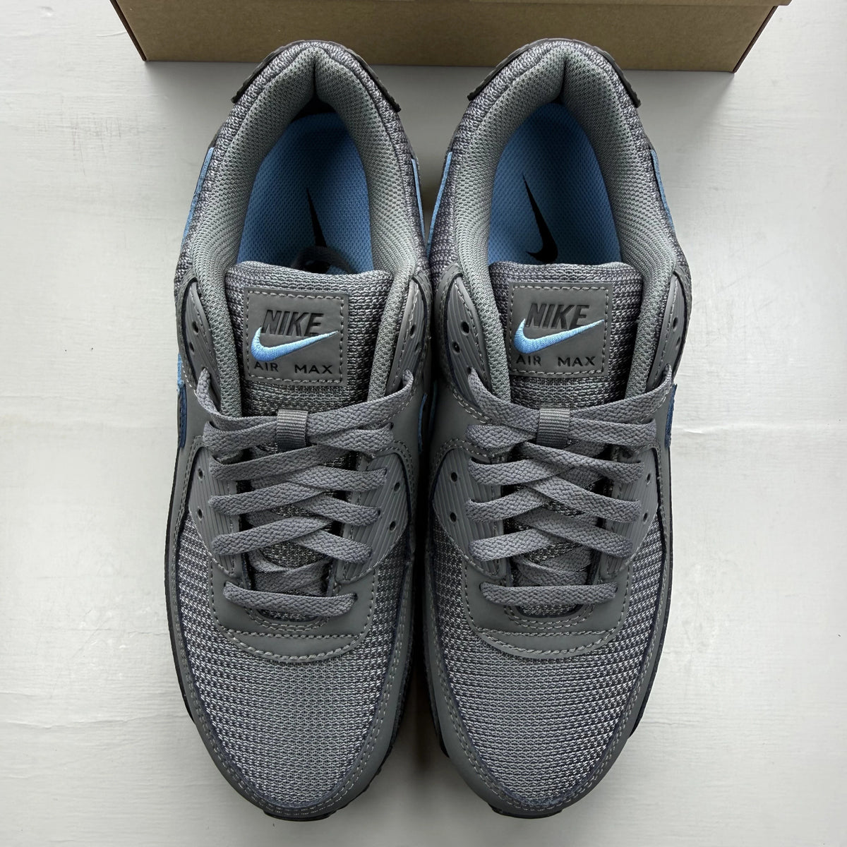 Nike Air Max 90 grey trainers with blue accents and logo detail.